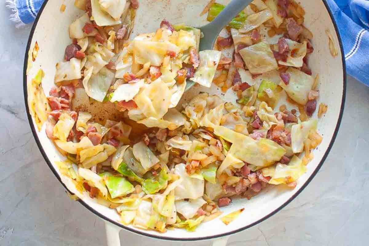 A skillet filled with sautéed cabbage, chopped bacon, and onions, mixed and cooked together.