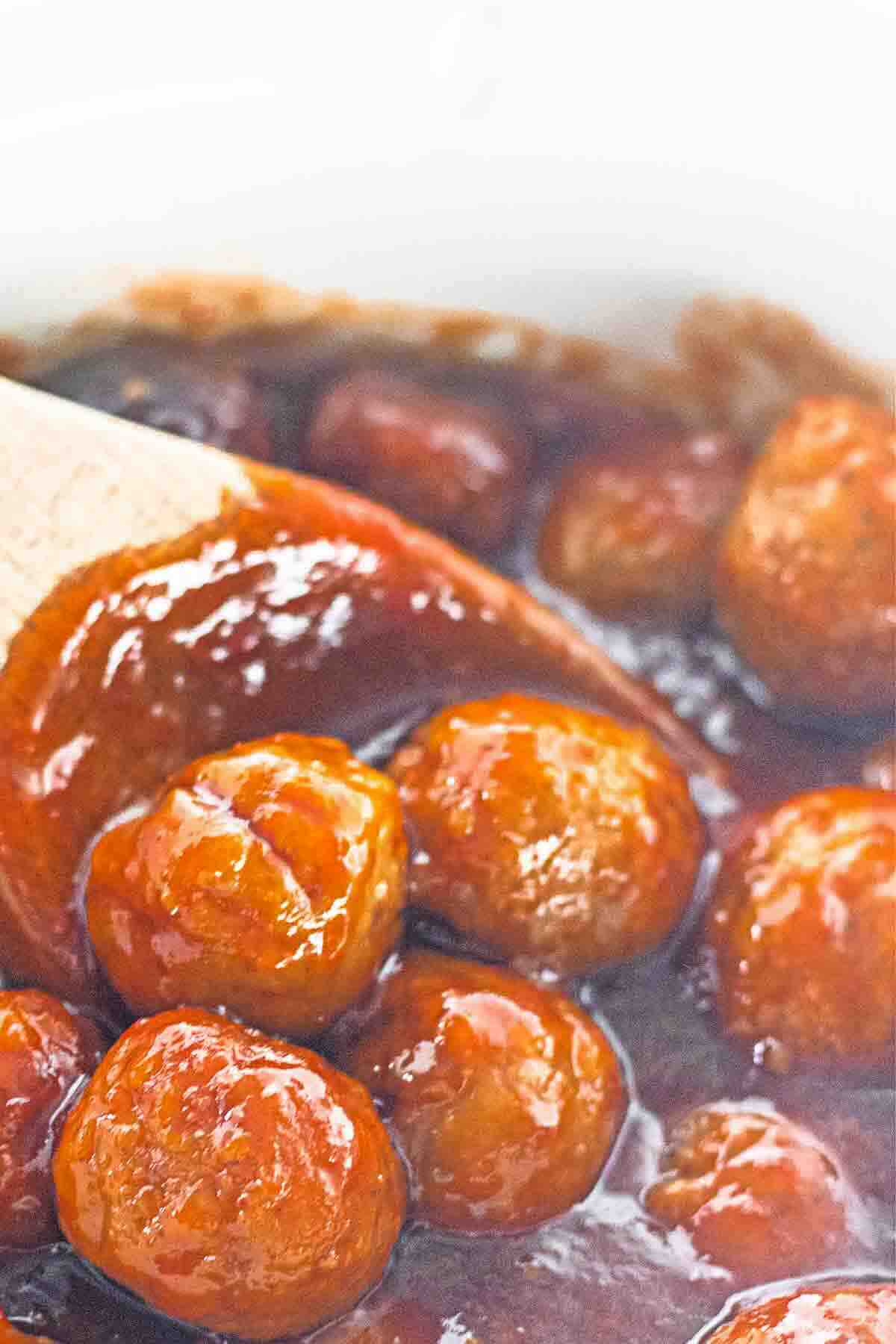 Meatballs coated in a thick red sauce, stirred with a wooden spoon.
