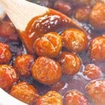 Meatballs coated in a thick, glossy brown sauce are being stirred with a wooden spoon in a pot.