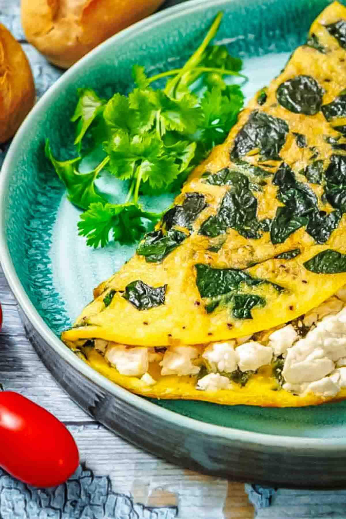 A folded omelet filled with feta cheese and spinach on a teal plate, garnished with fresh cilantro.
