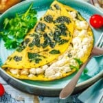 Folded spinach and feta cheese omelet on a teal plate with a side of cilantro and a fork.