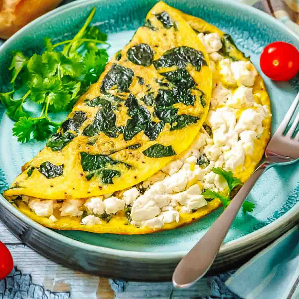 Folded spinach and feta cheese omelet on a teal plate with a side of cilantro and a fork.