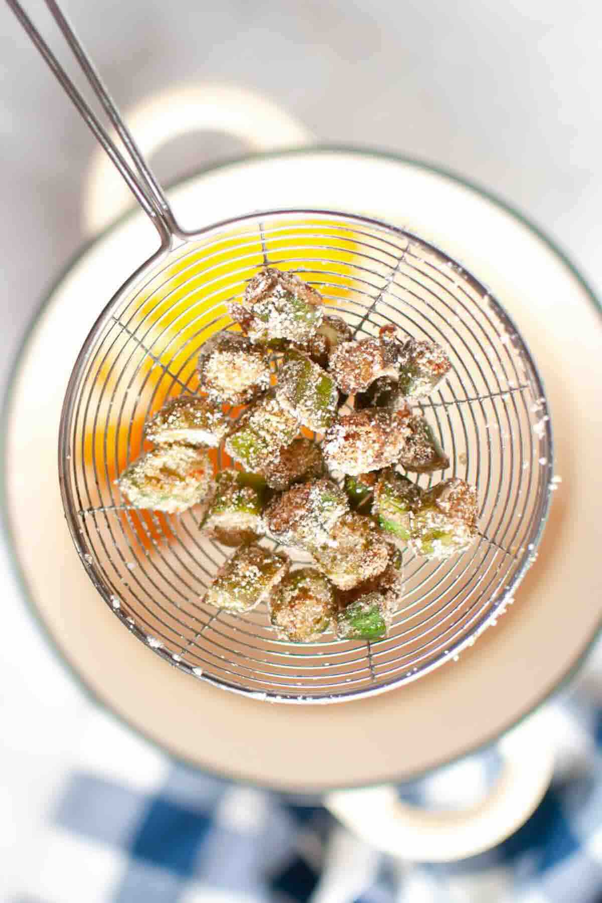Battered and fried okra pieces in a wire skimmer.