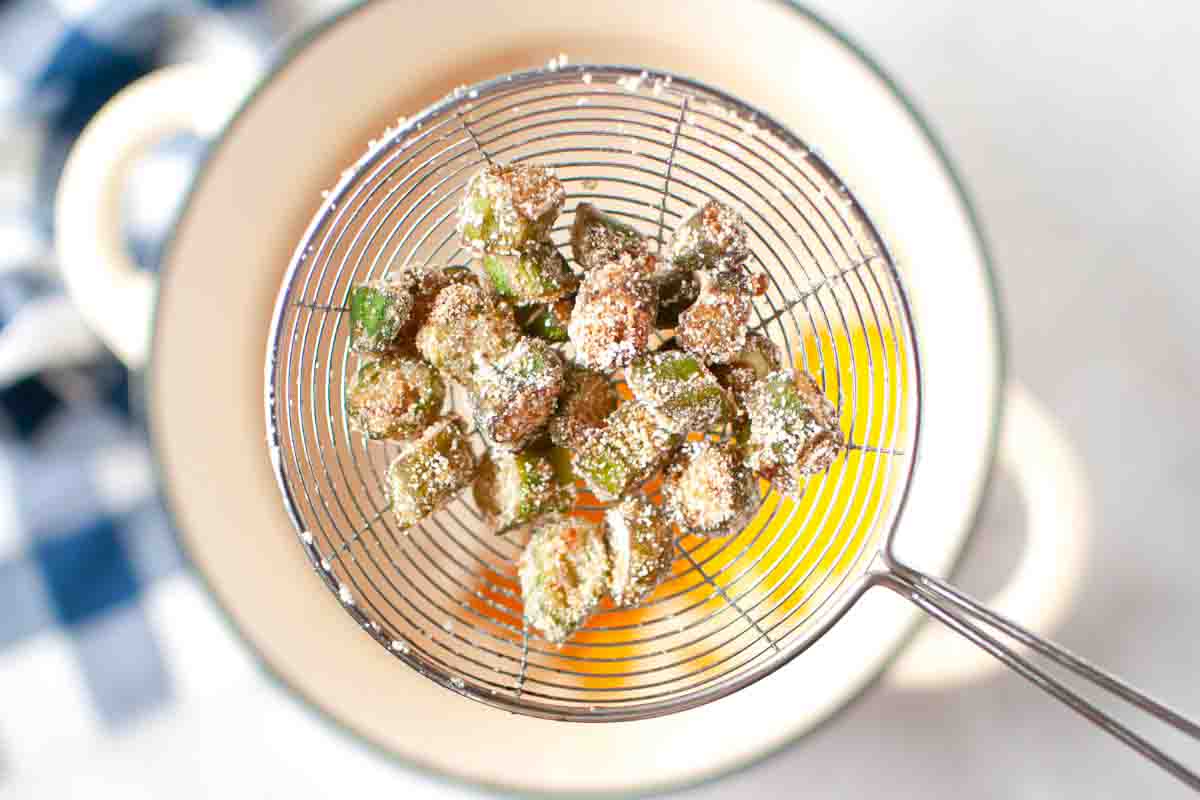 Battered and fried okra pieces in a wire mesh strainer held over a pot.