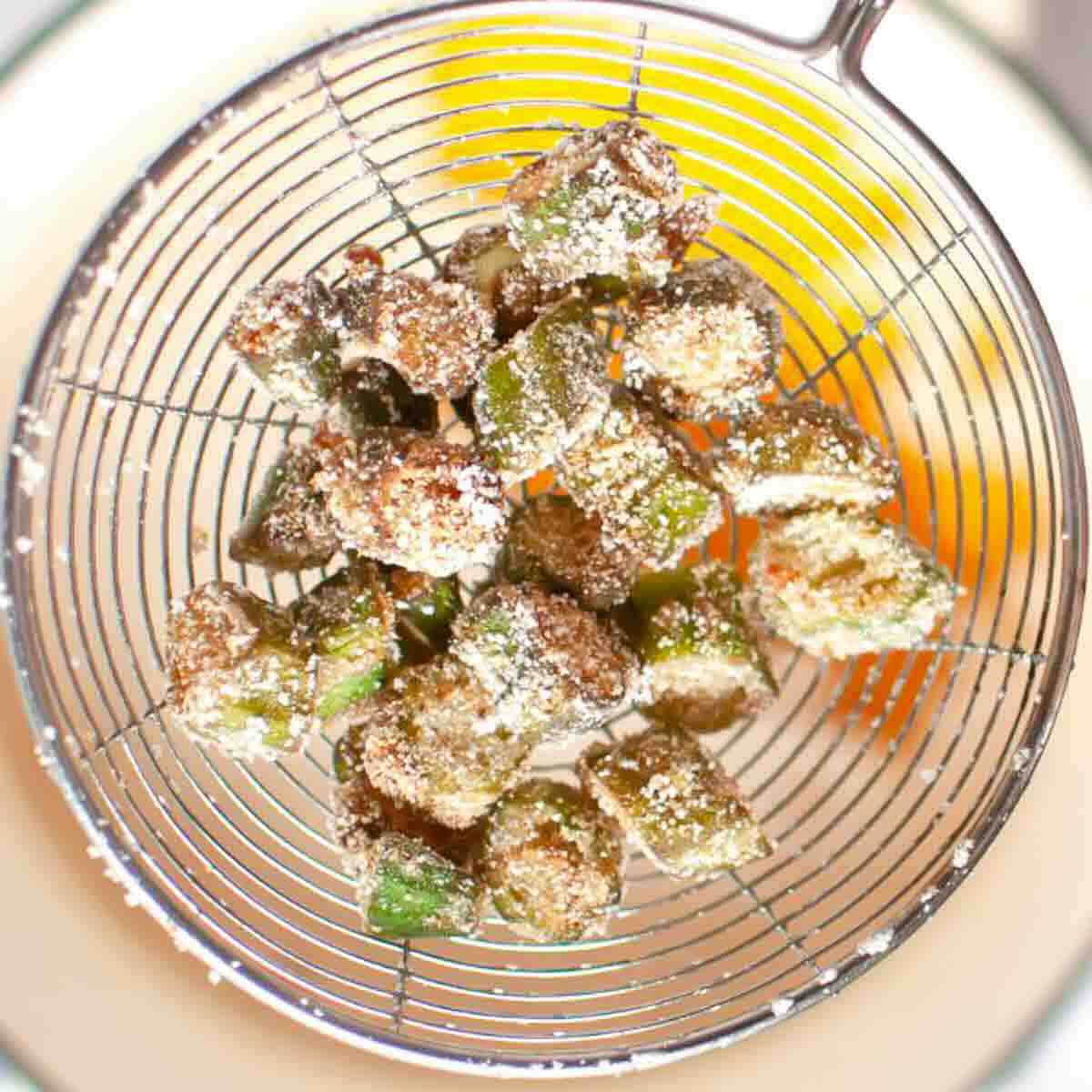 Breaded okra pieces in a wire mesh strainer.