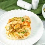 Two baked chicken breasts seasoned with herbs on a white scalloped plate.
