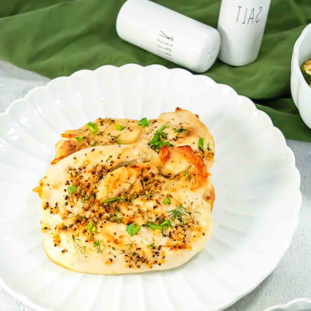 Two baked chicken breasts seasoned with herbs on a white scalloped plate.