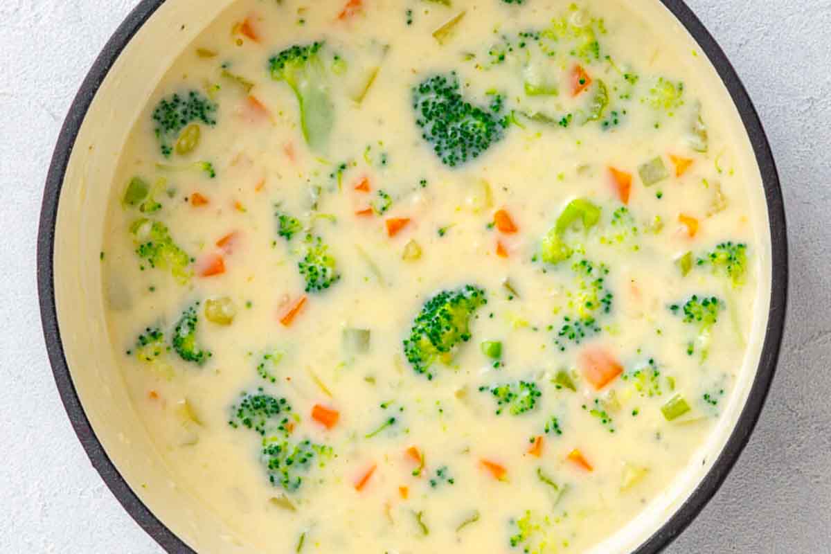 Creamy broccoli cheddar soup with diced carrots in a round pot.